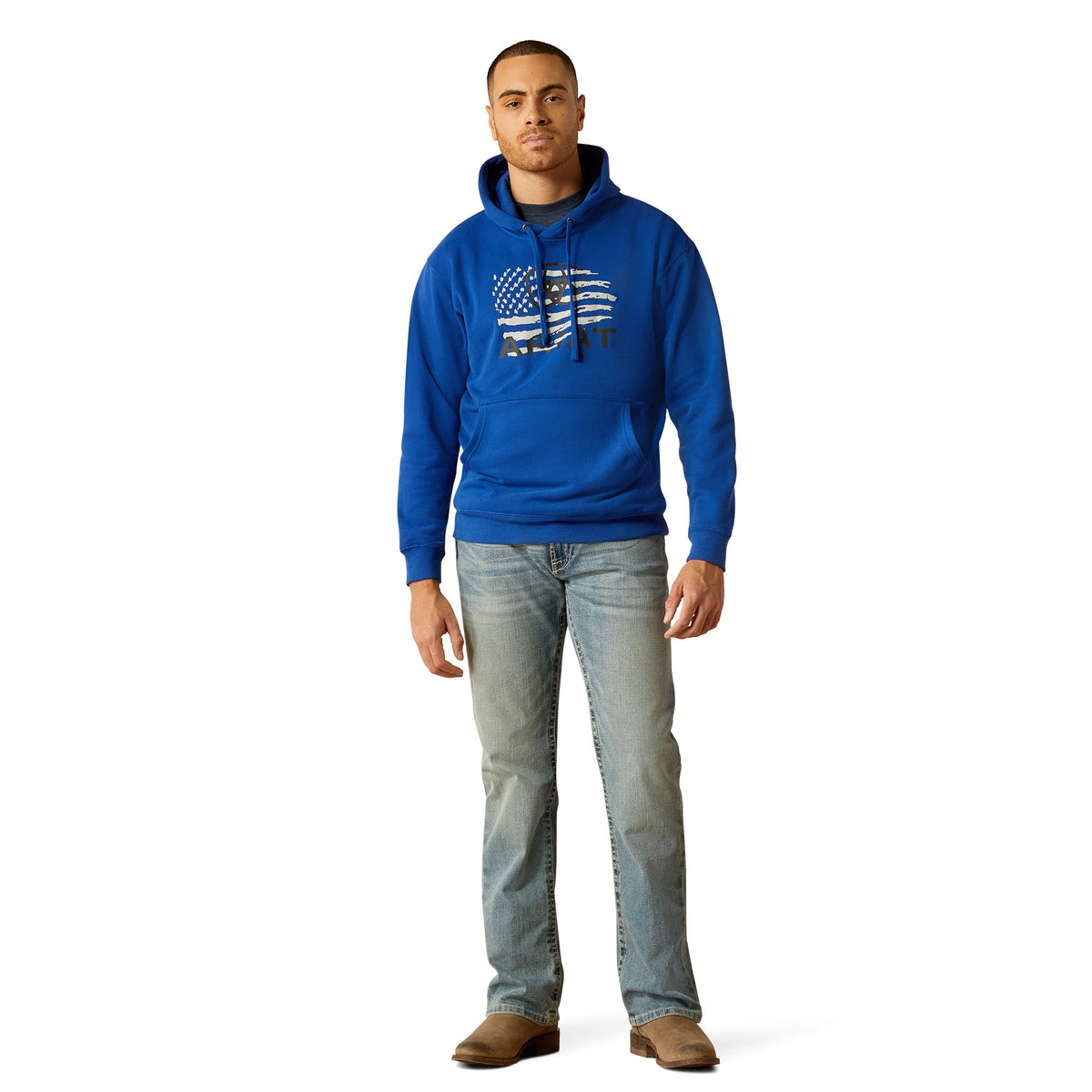 Man wearing a royal blue Ariat pullover hoodie with American flag graphic and light wash jeans
