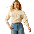 Woman wearing a cream Ariat logo crewneck sweatshirt with jeans and turquoise accessories
