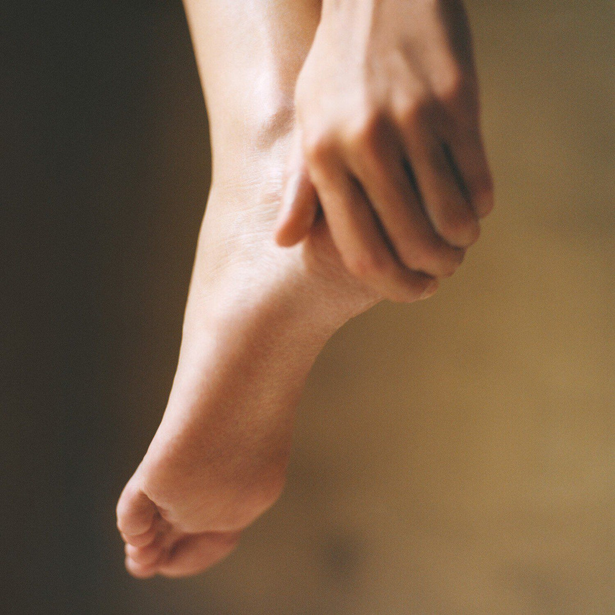Hand gently holding and massaging a bare foot, demonstrating foot care ritual technique