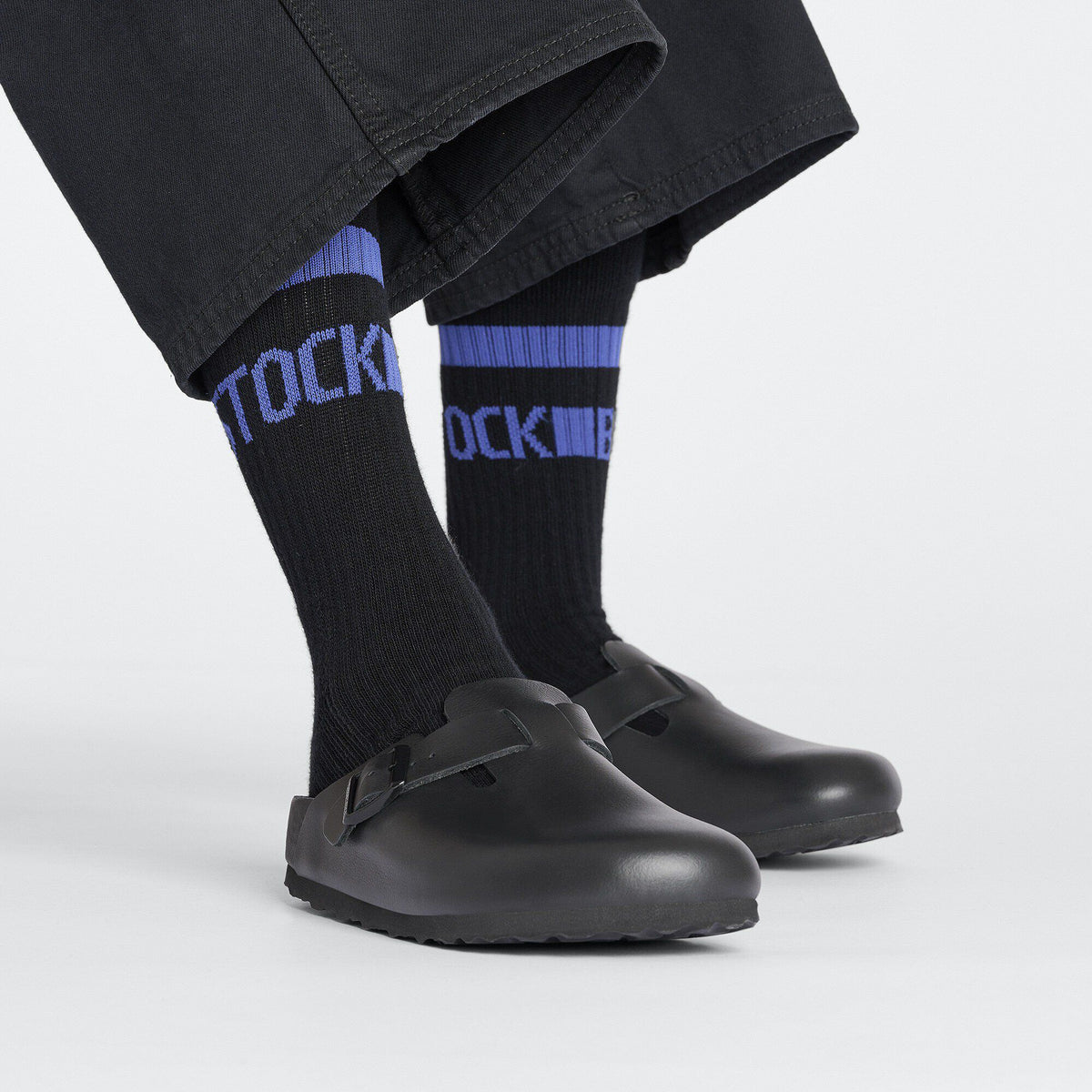 Black Birkenstock crew socks with blue stripes worn with black clogs and dark trousers
