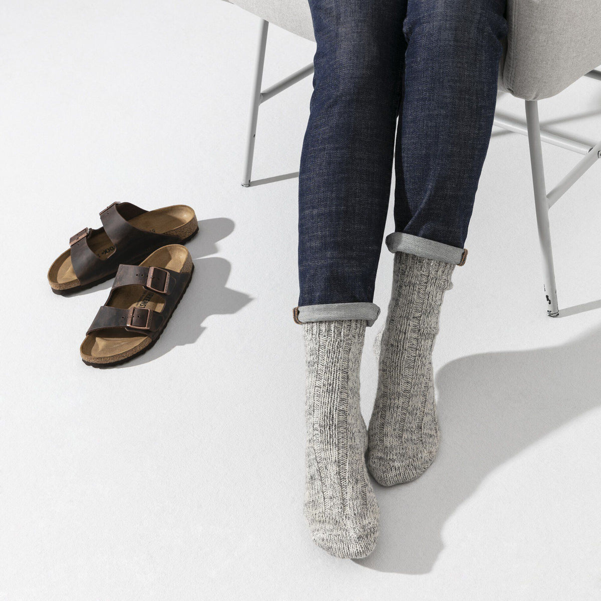 Person seated wearing light gray knit cotton socks with rolled denim jeans, Birkenstock sandals nearby