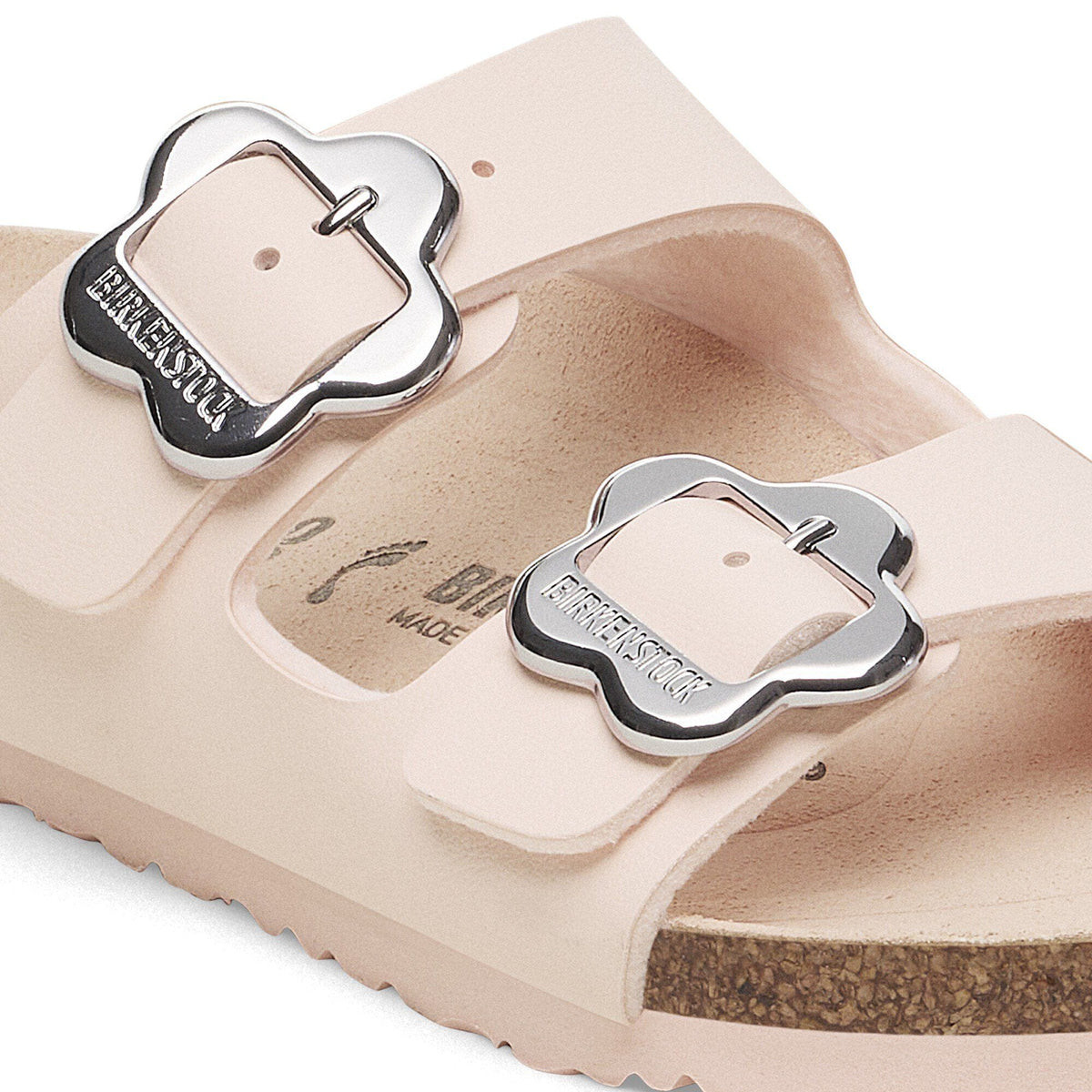 Close-up detail of Birkenstock kids sandal showing two silver flower-shaped buckles on pale pink straps