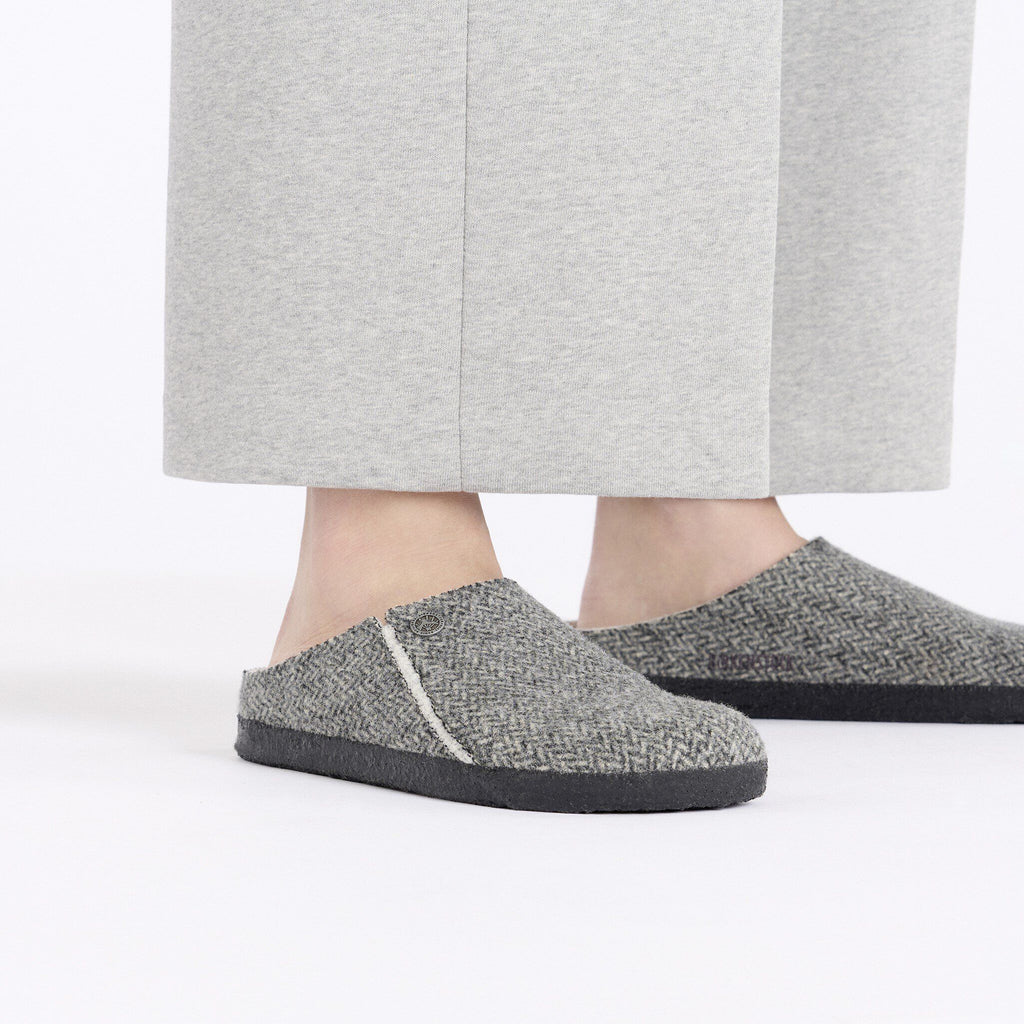 Person wearing gray herringbone slip-on clogs with dark rubber soles and shearling lining