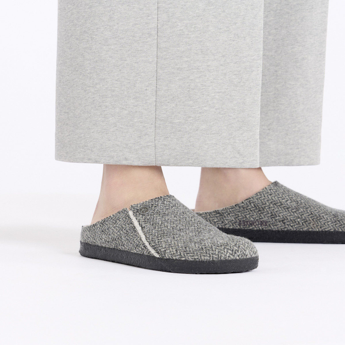 Person wearing gray herringbone slip-on clogs with dark rubber soles and shearling lining