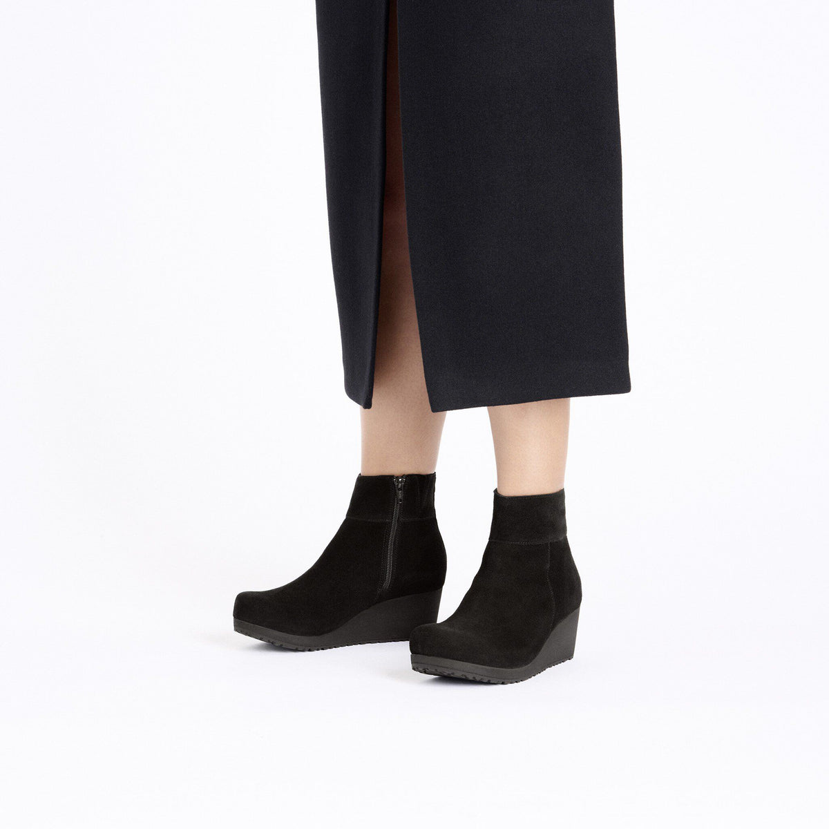 Woman wearing black suede wedge ankle boots with side zipper under a dark midi skirt