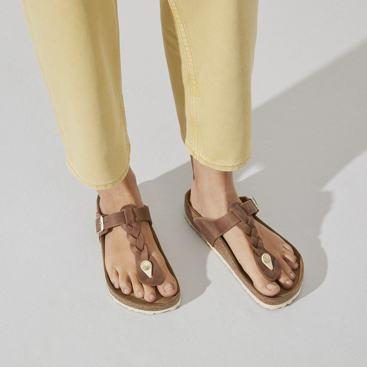 Woman wearing braided leather thong sandals with buckle strap and cork footbed