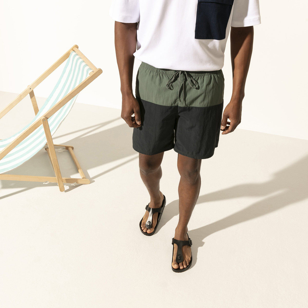 Model wearing black Birkenstock Gizeh EVA thong sandals with beach chair in background