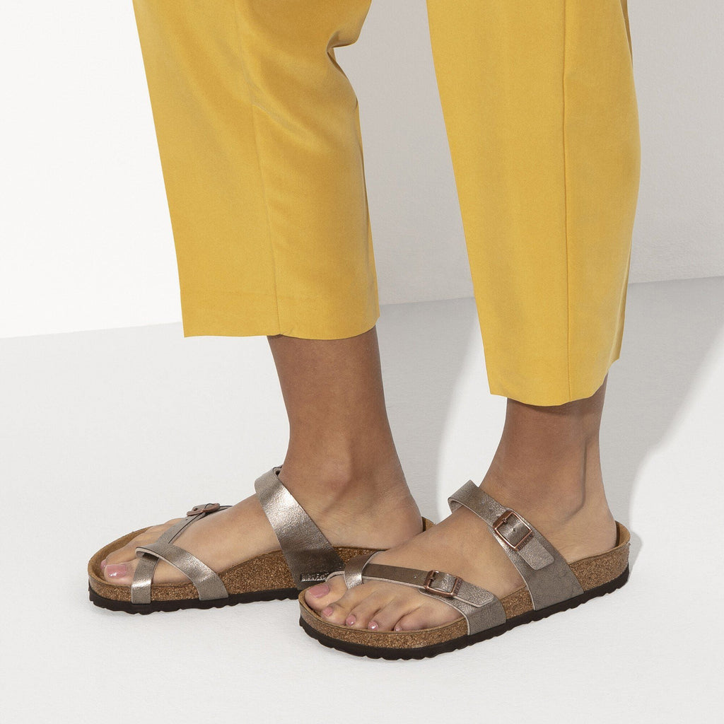 Woman wearing taupe metallic Birkenstock Mayari thong sandals with cork footbed and yellow cropped trousers