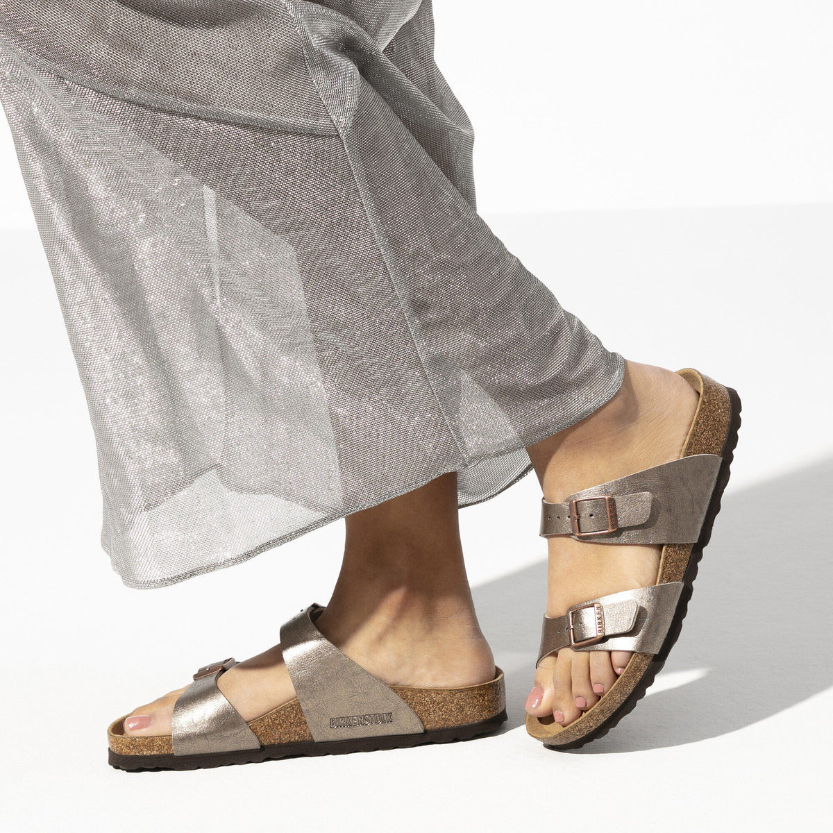 Woman wearing Birkenstock two-strap sandals with cork footbed and metallic taupe straps