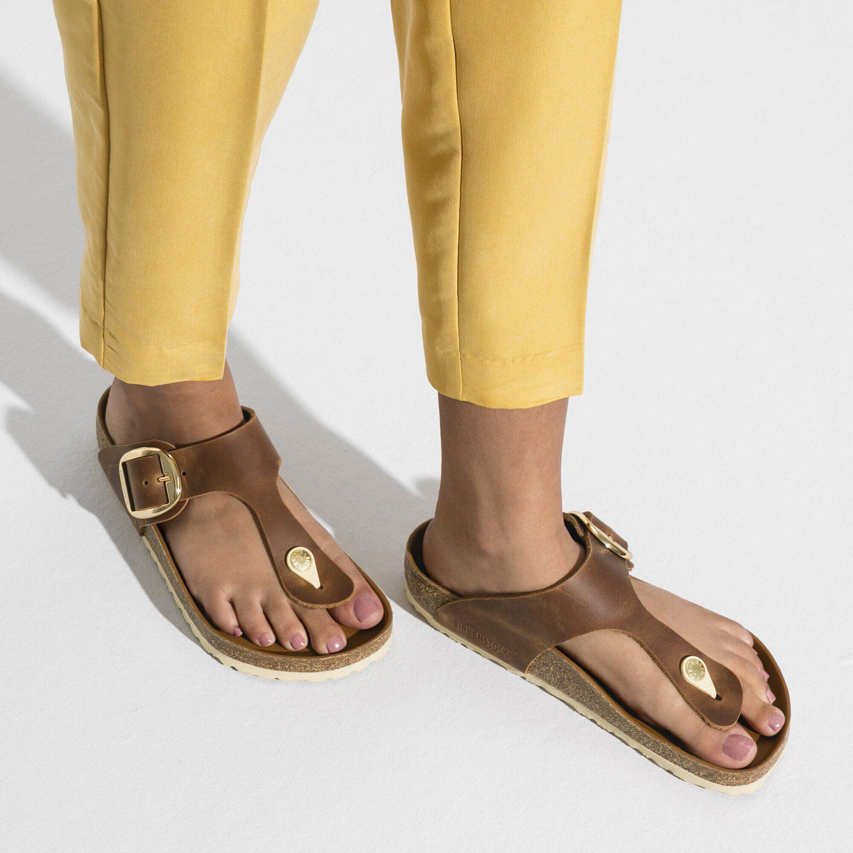 Woman wearing brown leather Birkenstock Gizeh thong sandals with gold buckle detail
