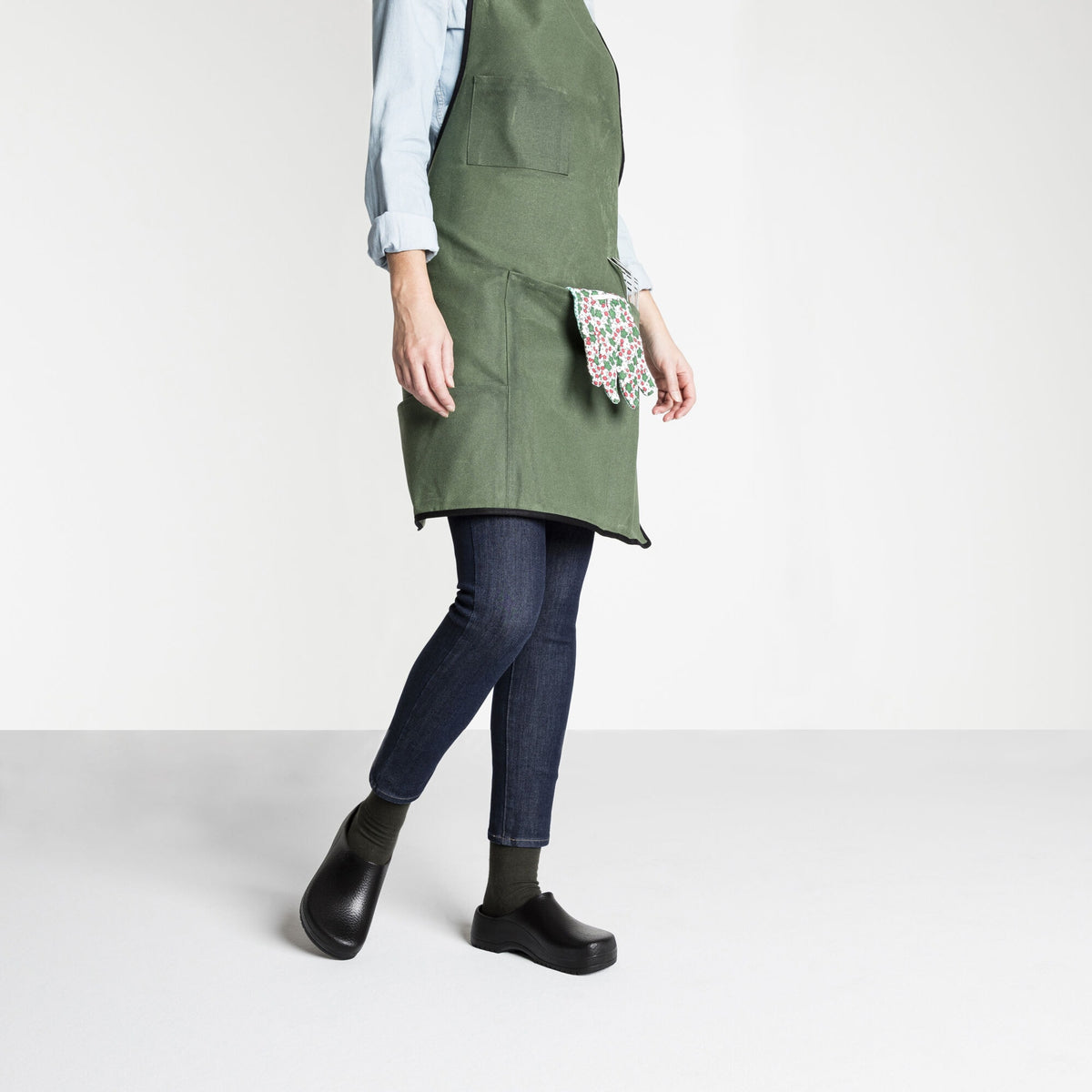 Woman wearing black Birkenstock Super Birki clogs with green apron and dark jeans