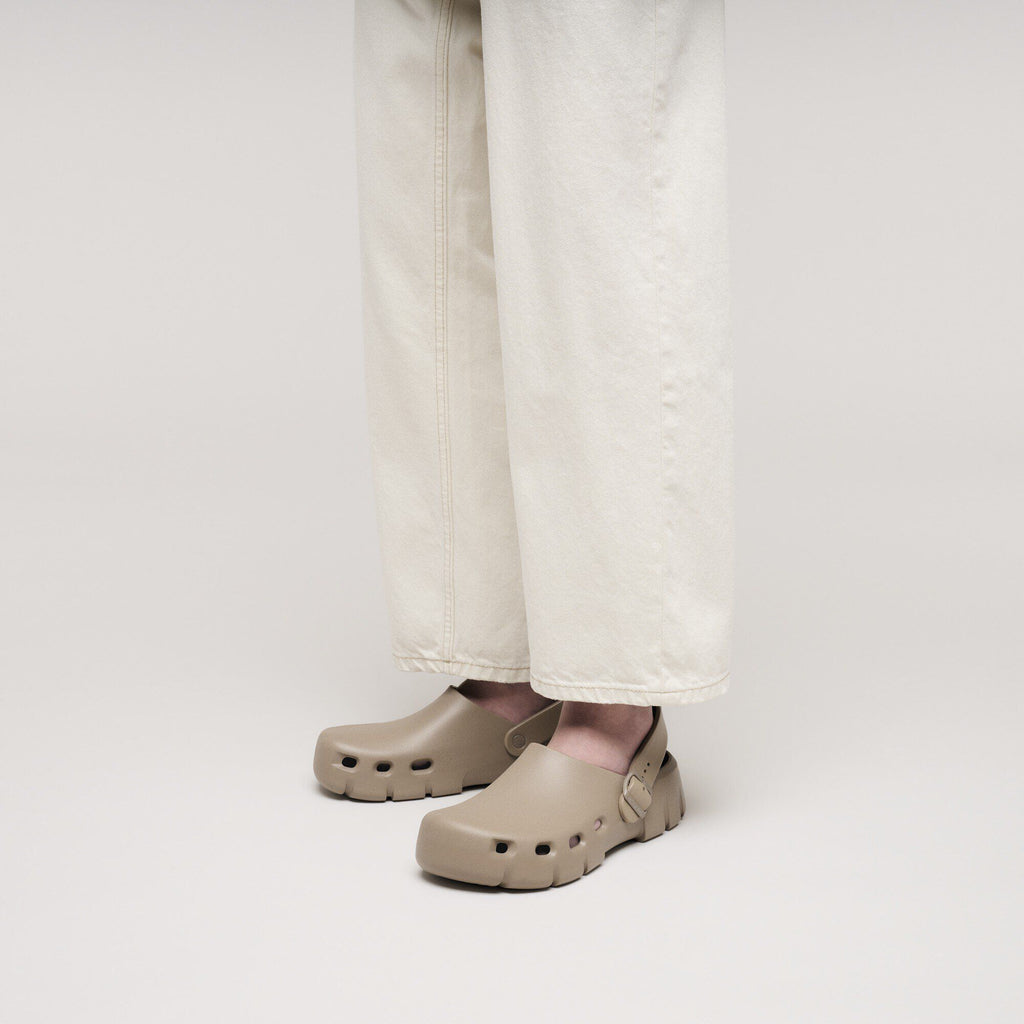 Model wearing Birkenstock Birki Flow clogs with buckle strap, paired with wide-leg cream trousers
