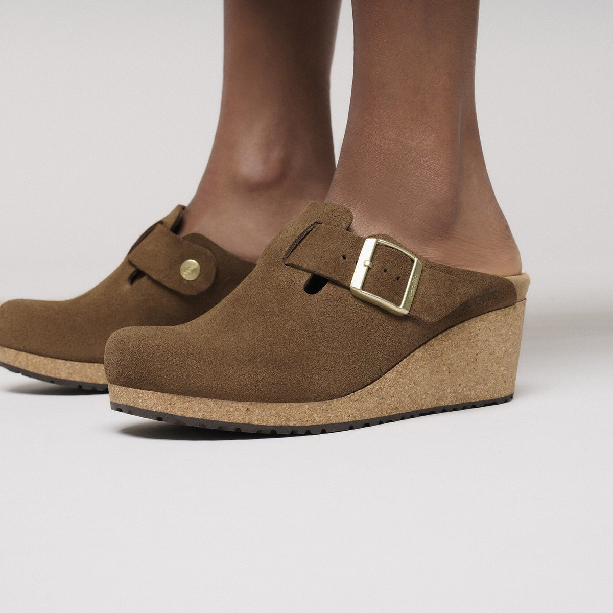 Womens Birkenstock suede wedge clogs with gold buckle and cork sole, worn on feet