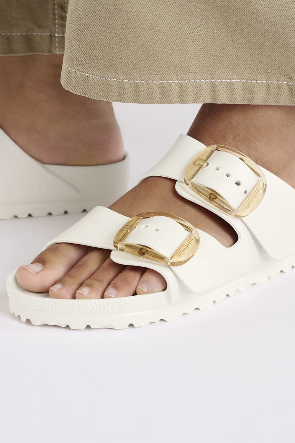 Close-up of white Birkenstock Arizona Big Buckle EVA sandals with gold oversized buckles worn on feet