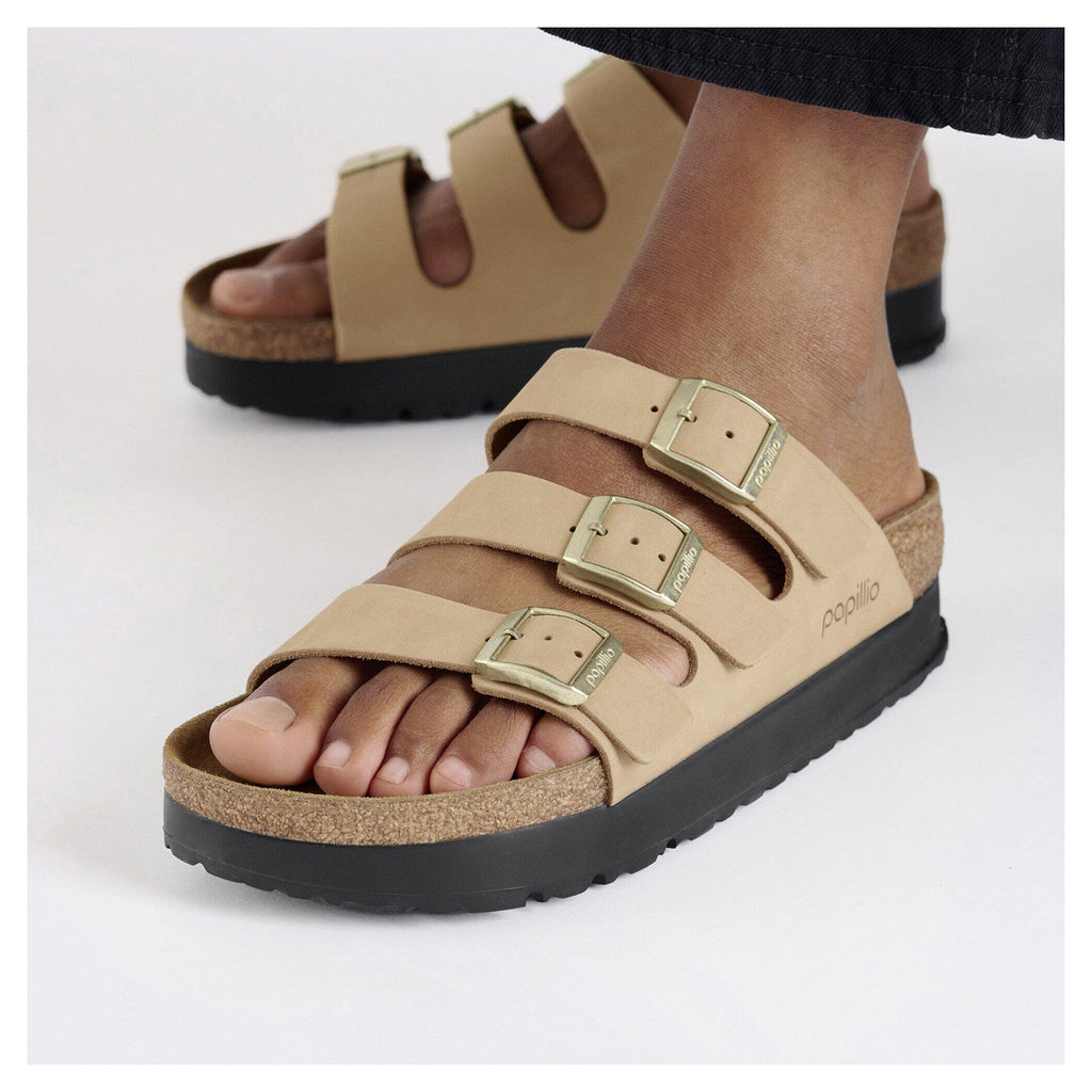 Woman wearing three-strap platform sandals with gold buckles and cork footbed