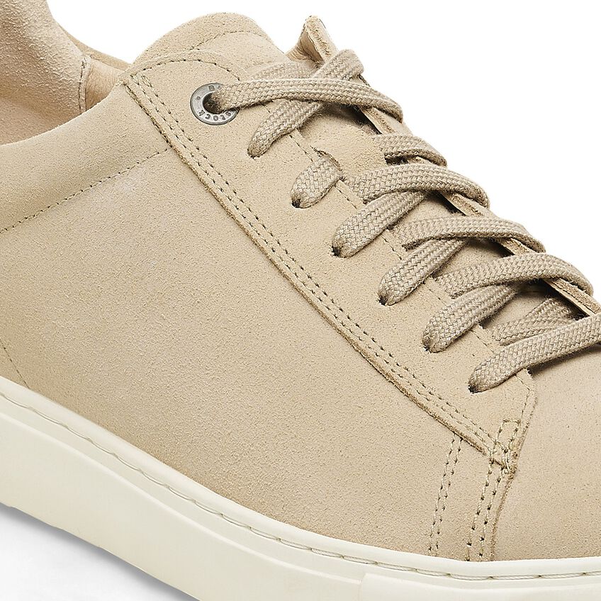 Close-up detail of a beige suede low-top sneaker with matching laces and white sole