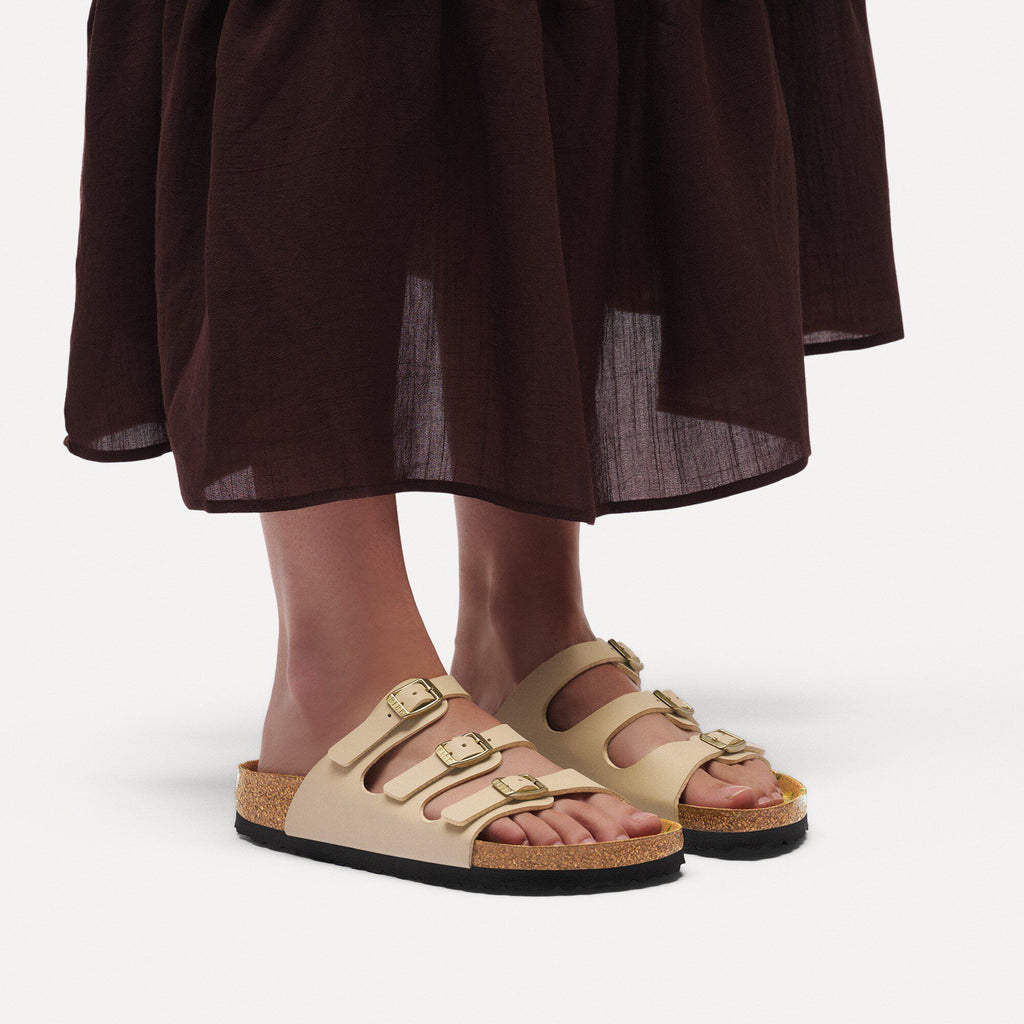 Woman wearing beige three-strap Birkenstock Florida sandals with gold buckles and cork sole
