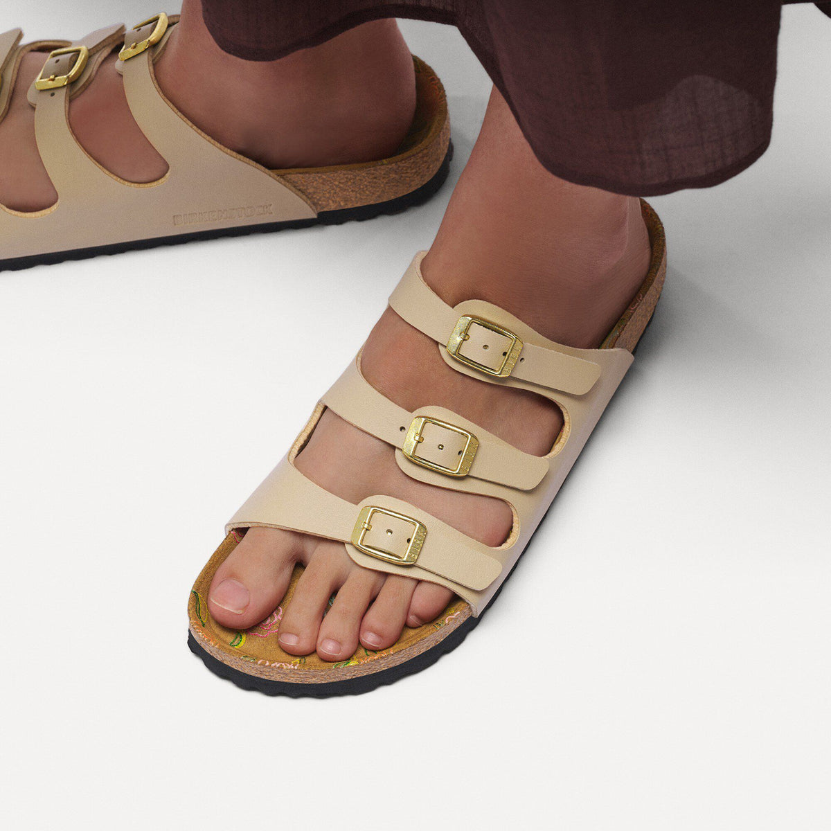Woman wearing three-strap Birkenstock Florida sandals with gold buckles on seamless background