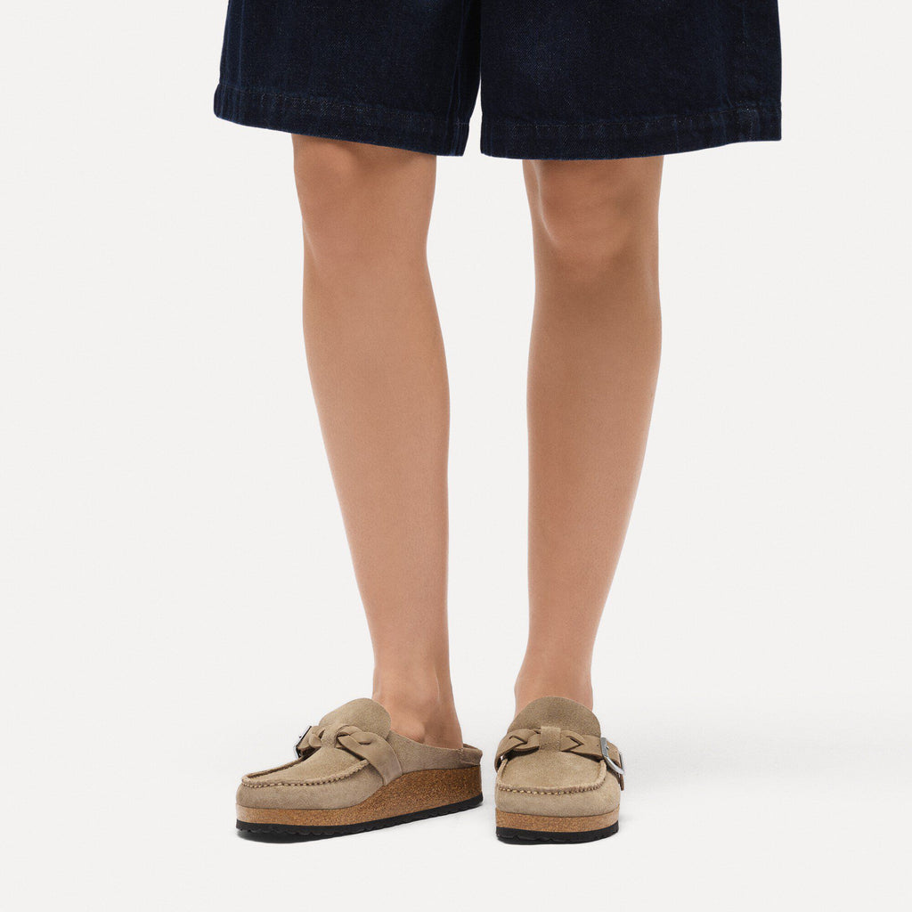 Woman wearing taupe suede Birkenstock Buckley Braided mule clogs with dark denim shorts