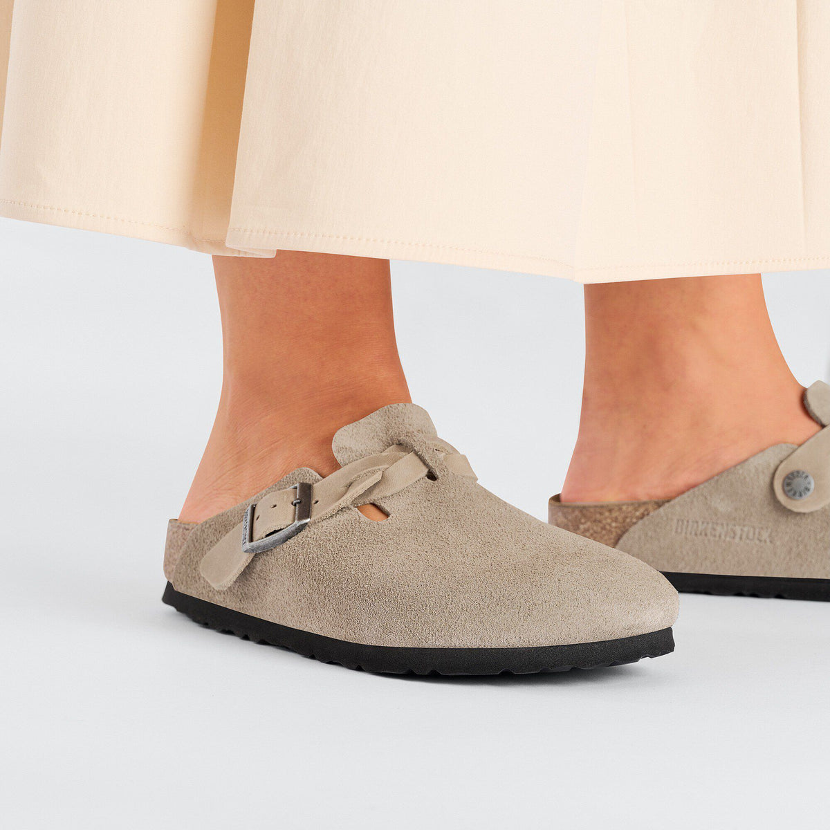 Woman wearing closed-toe suede Birkenstock clogs with braided strap and buckle detail