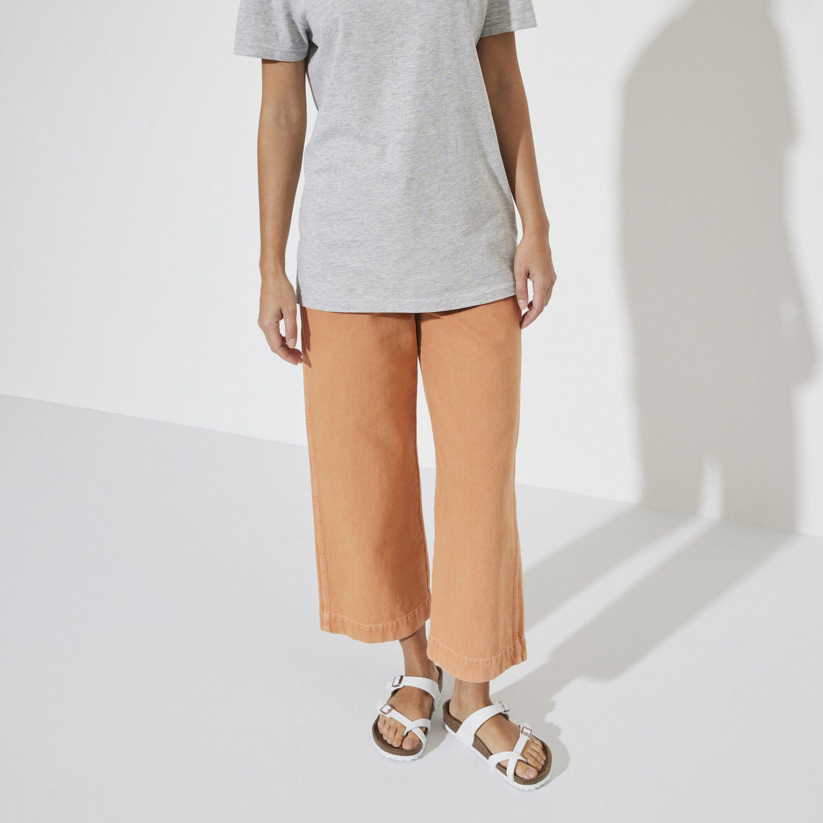 Model wearing white Birkenstock Mayari sandals with orange wide-leg cropped pants