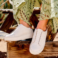 Women wearing white slip-on leather sneakers with elastic bands, paired with embroidered green trousers