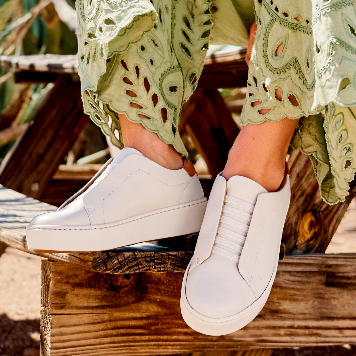 Women wearing white slip-on leather sneakers with elastic bands, paired with embroidered green trousers