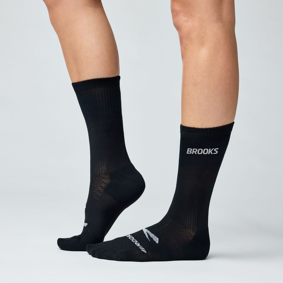 Brooks crew-length black running socks shown on model legs from two angles