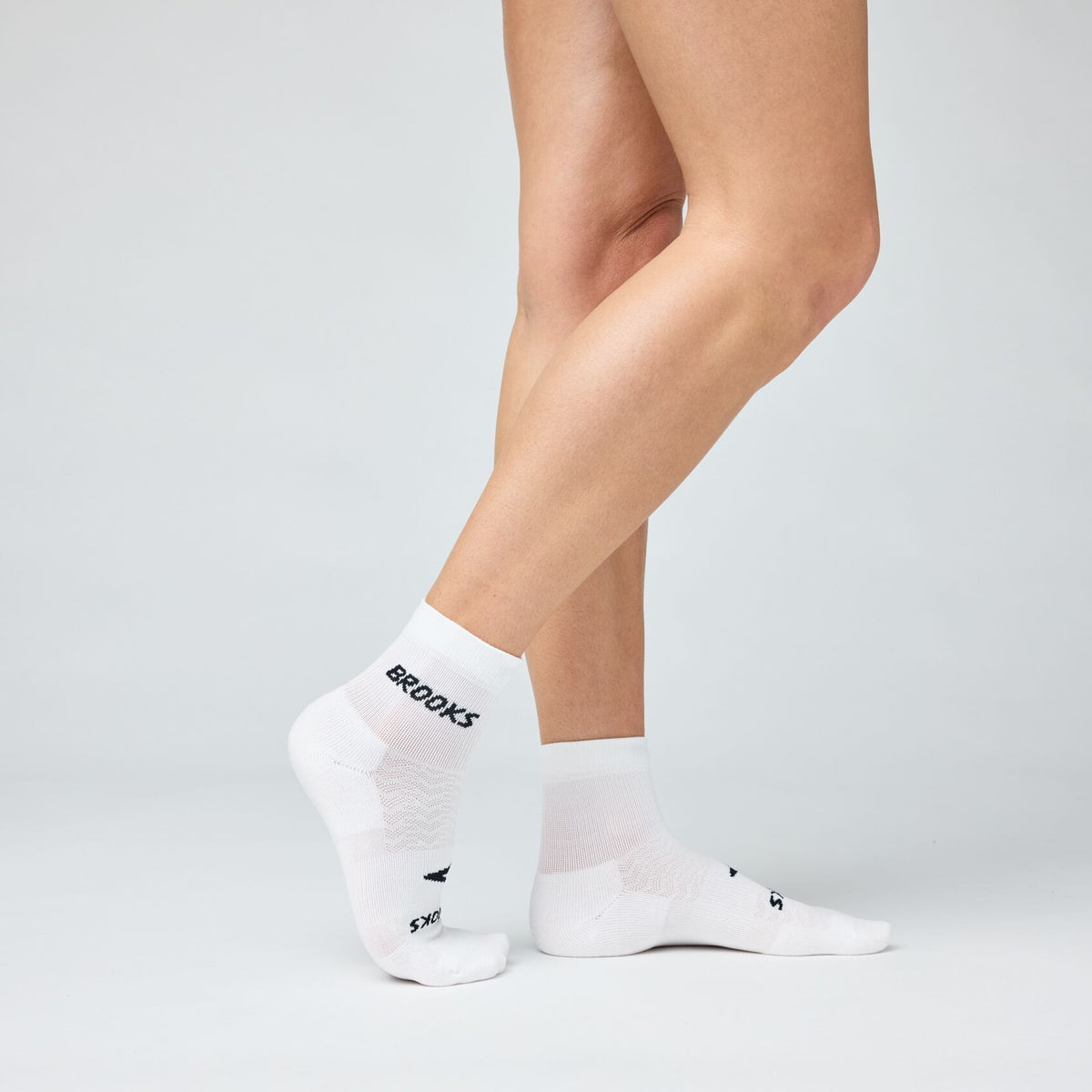 Model wearing white Brooks quarter-length running socks shown from two angles on lower legs