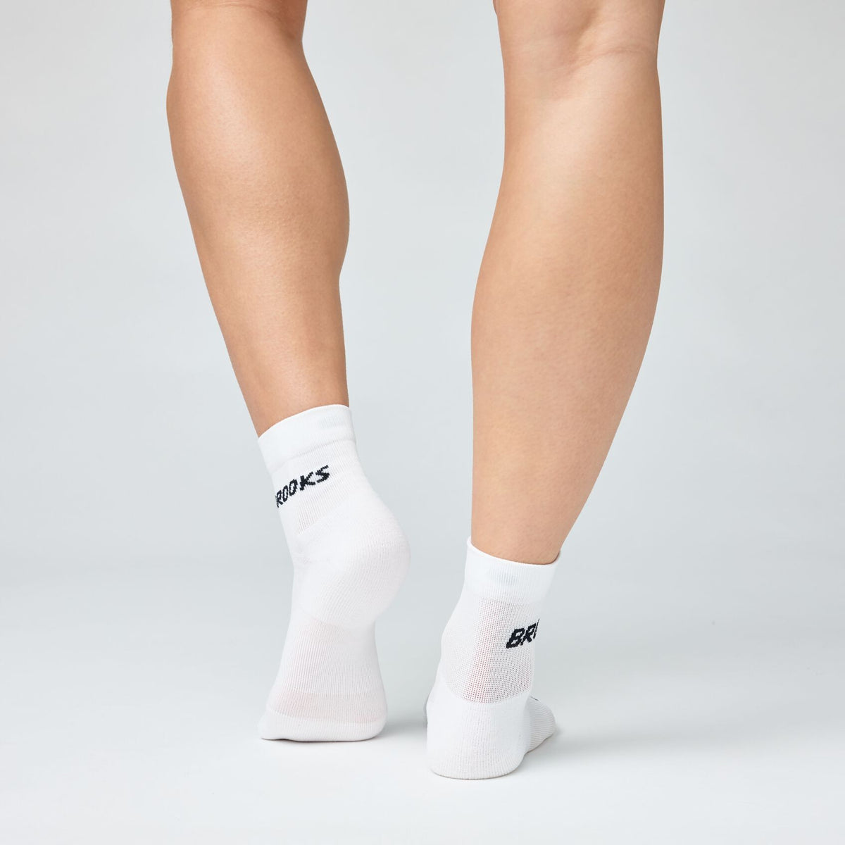 Back view of legs wearing white Brooks quarter-length running socks with black logo
