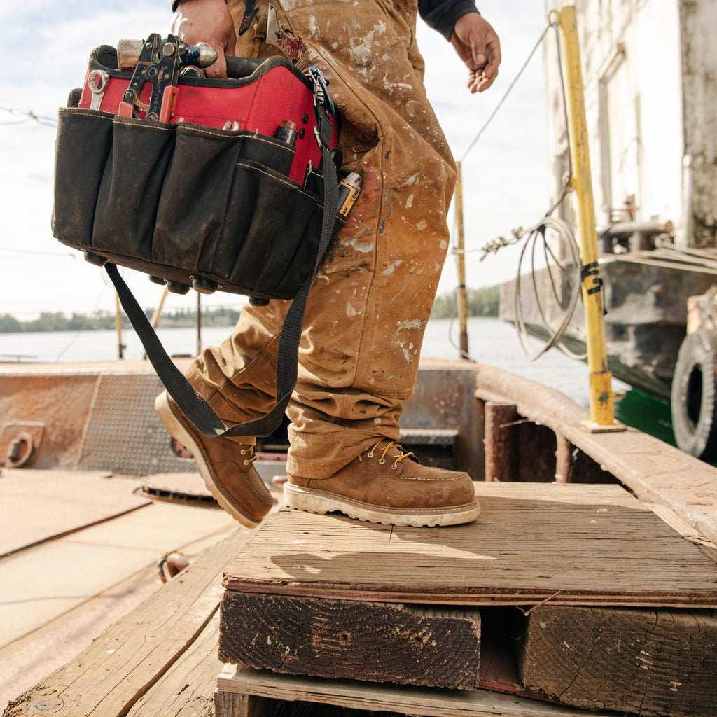 Worker wearing brown moc toe work boots stepping up on wooden planks at a dock worksite