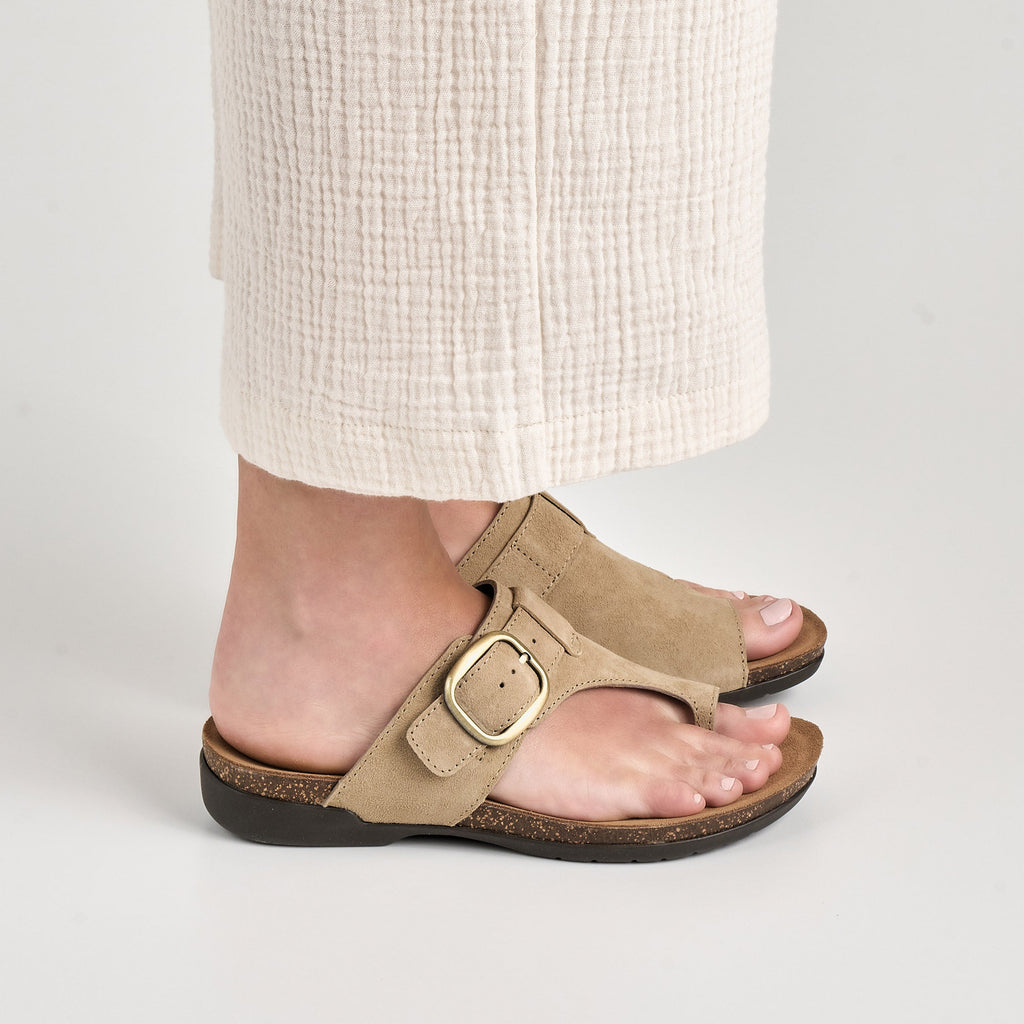 Woman wearing taupe suede toe-post sandals with gold buckle and cork footbed
