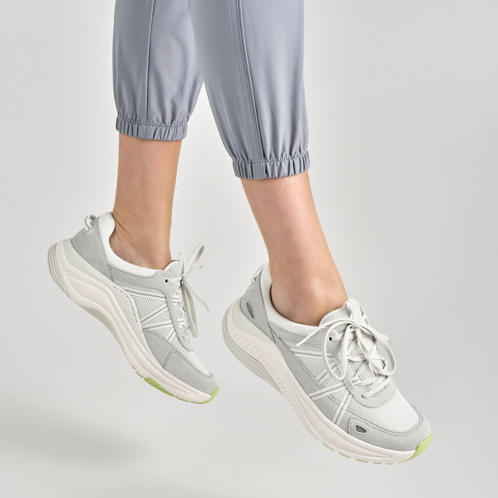 Woman wearing grey suede lace-up sneakers with chunky white sole, shown mid-air
