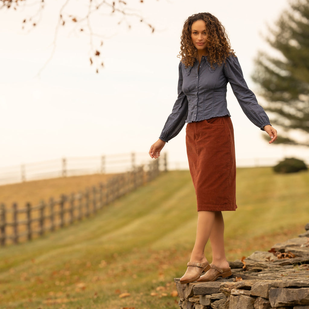 Woman balancing on stone wall wearing tan Mary Jane clogs with buckle strap outdoors