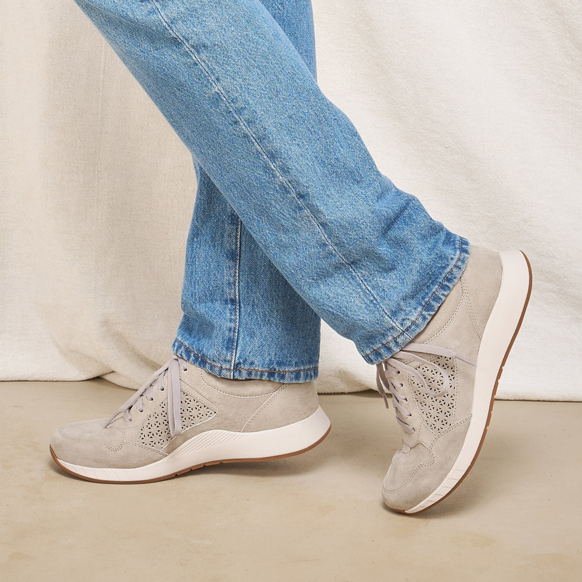 Woman wearing grey suede lace-up sneakers with laser-cut floral detail and white sole