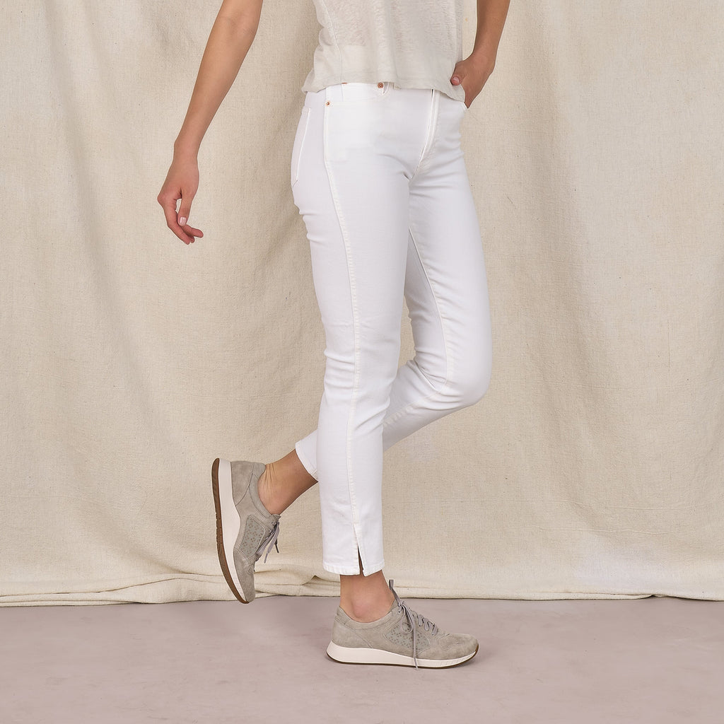 Woman wearing grey suede lace-up sneakers with white cropped jeans, side view