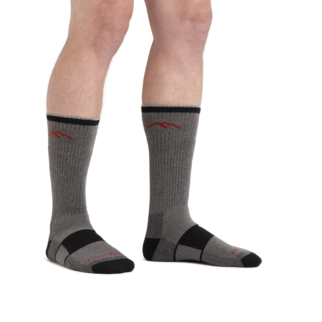 Model wearing gray and black Darn Tough boot socks with red mountain logo, front view
