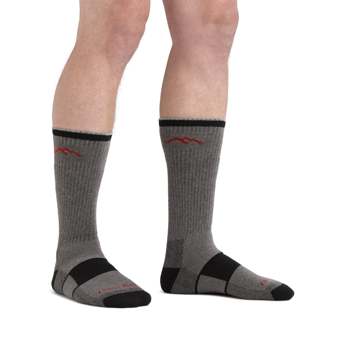 Model wearing gray and black Darn Tough boot socks with red mountain logo, front view