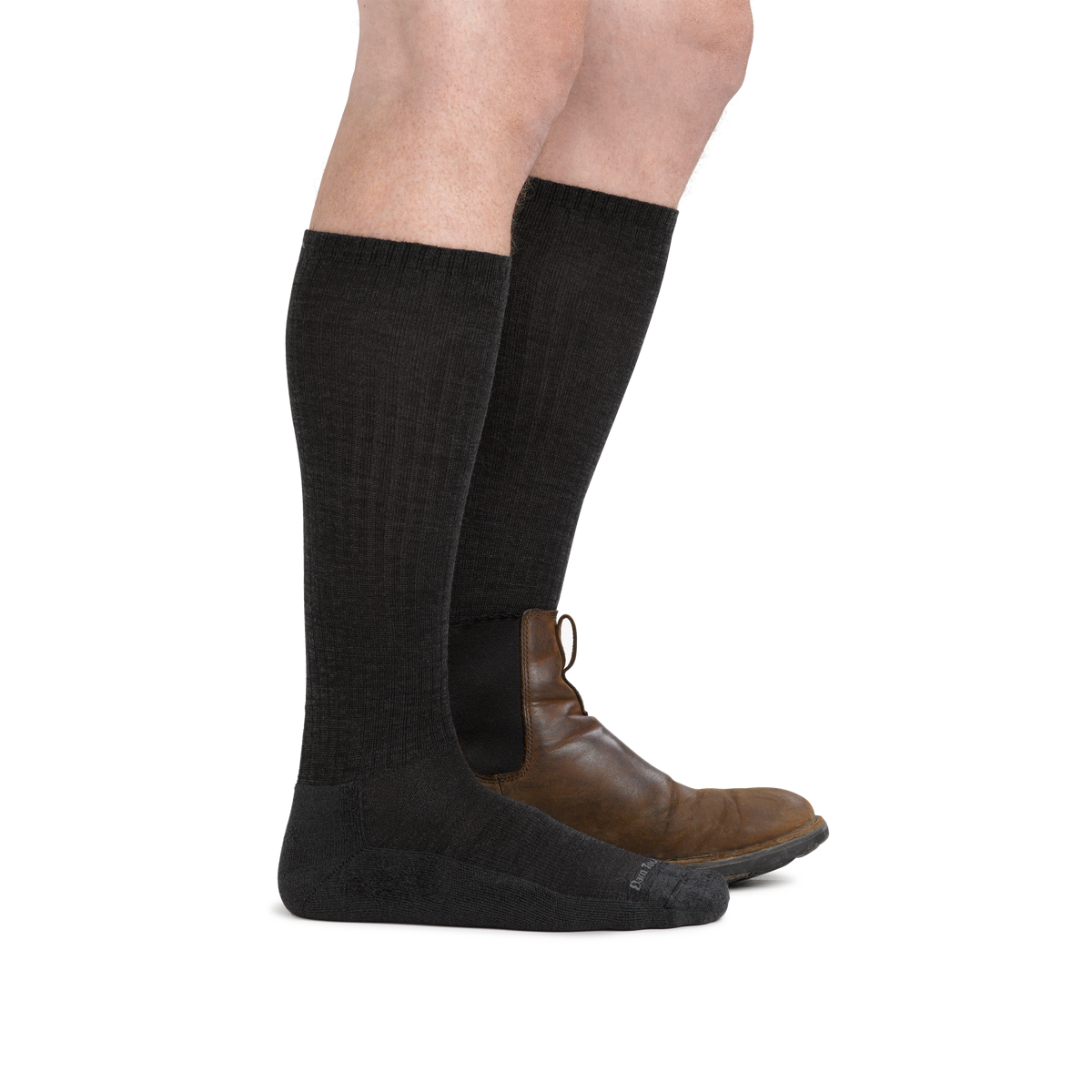 Side view of legs wearing tall black wool socks with brown Chelsea boots