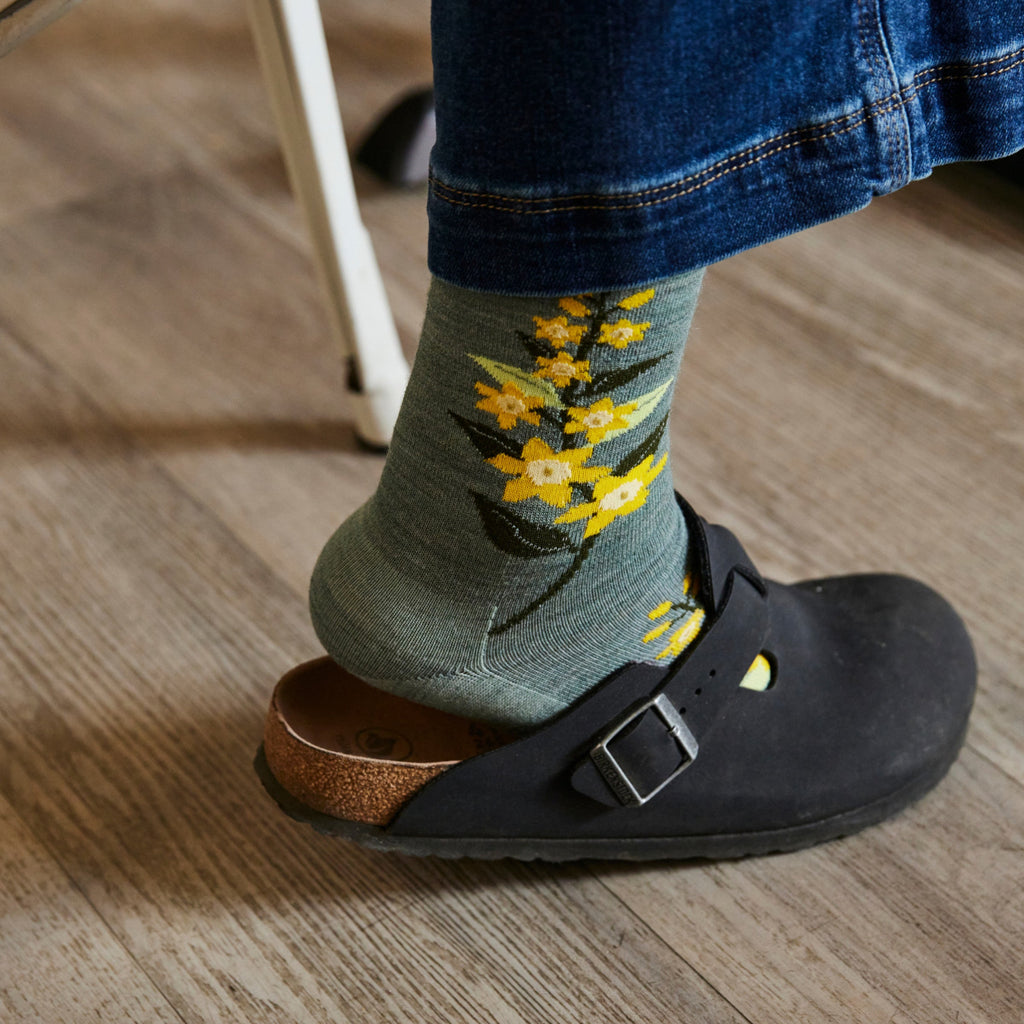 Sage green floral crew socks with yellow blossoms worn with black Birkenstock clogs and jeans