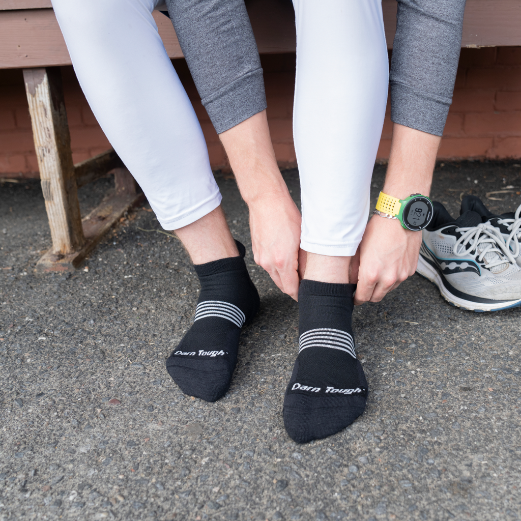 Person adjusting Darn Tough no-show tab running socks before putting on athletic shoes