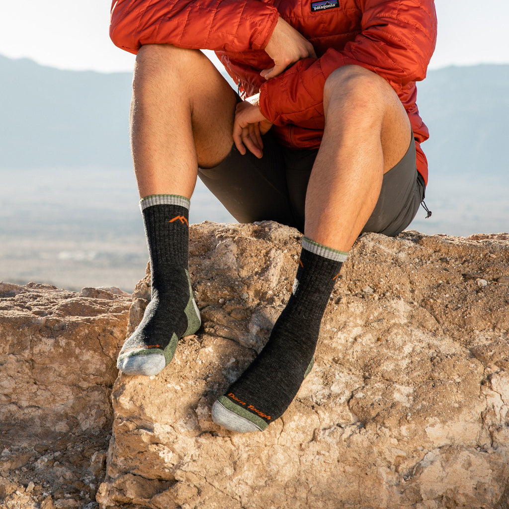 Person sitting on rocky outcrop wearing Darn Tough micro crew cushion hiking socks outdoors