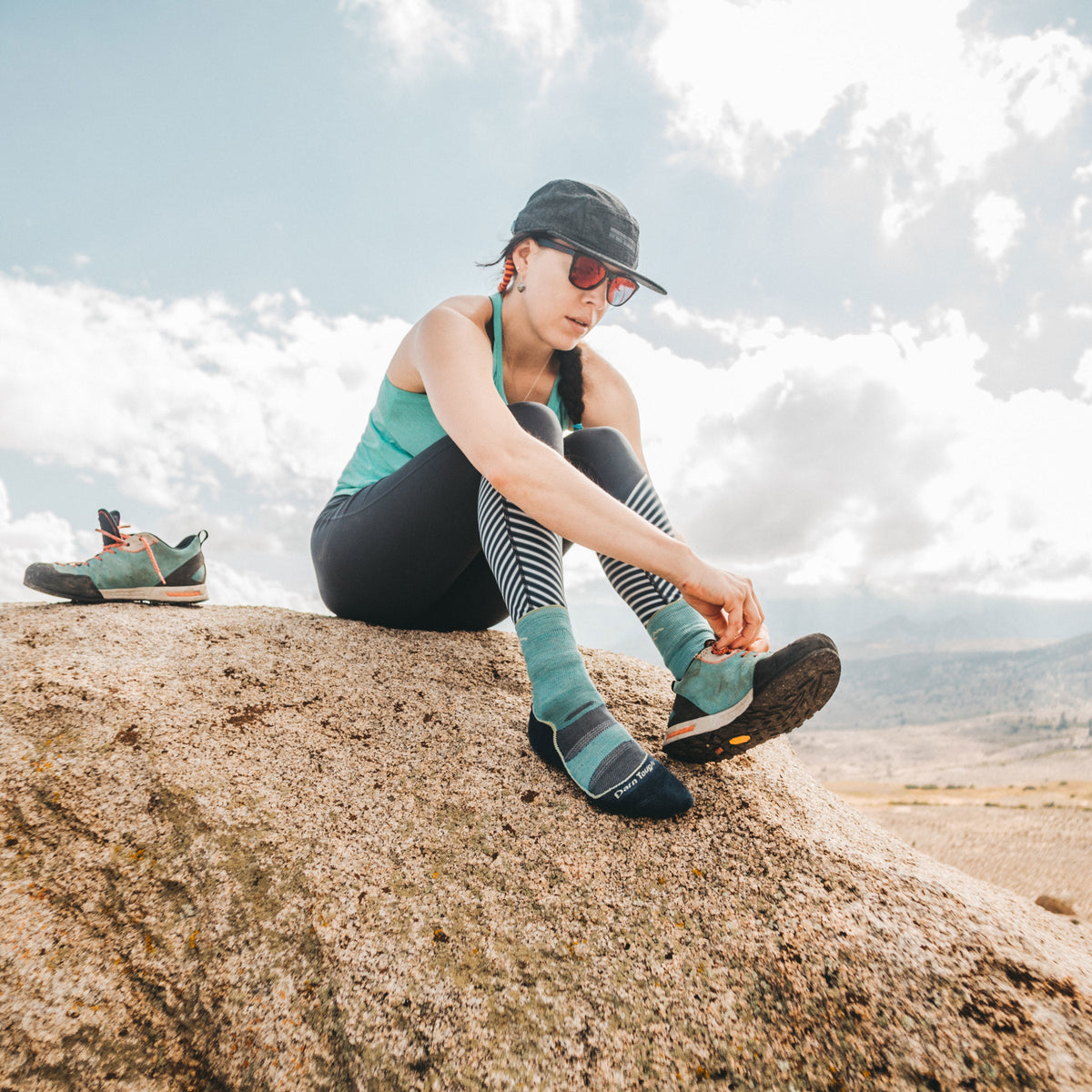 Woman sitting on a boulder adjusting her hiking shoe wearing Darn Tough crew socks outdoors