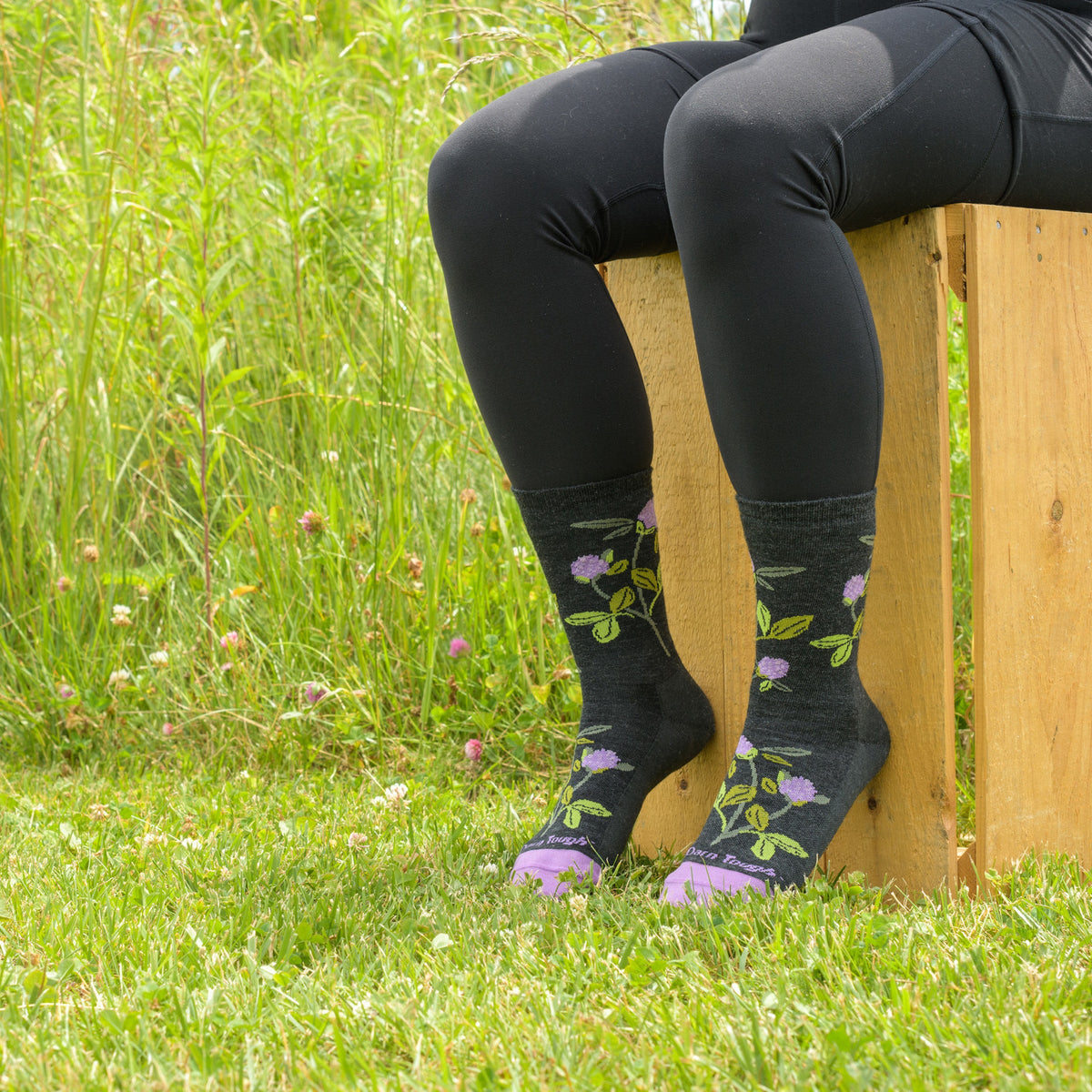 Person seated outdoors wearing charcoal crew socks with floral clover pattern on grass