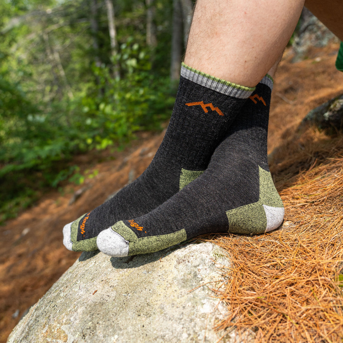 Darn Tough micro crew cushion socks worn on feet resting on a rock in a forest setting