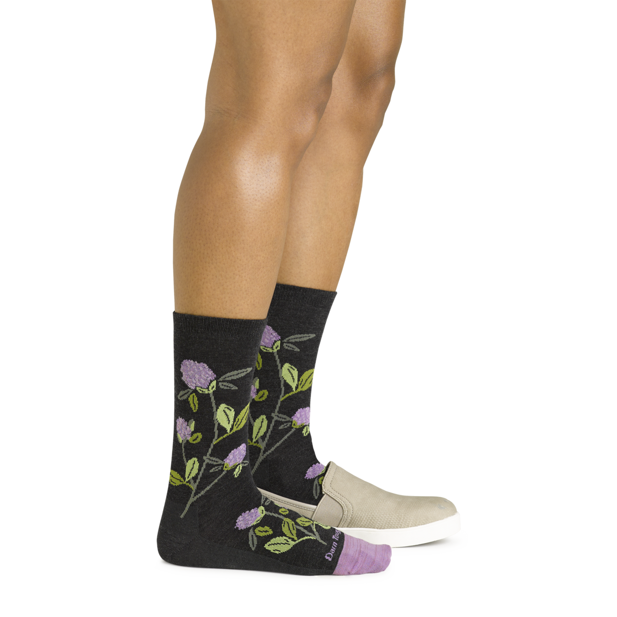 Woman wearing dark charcoal crew socks with purple floral and green leaf pattern, paired with beige slip-on shoes
