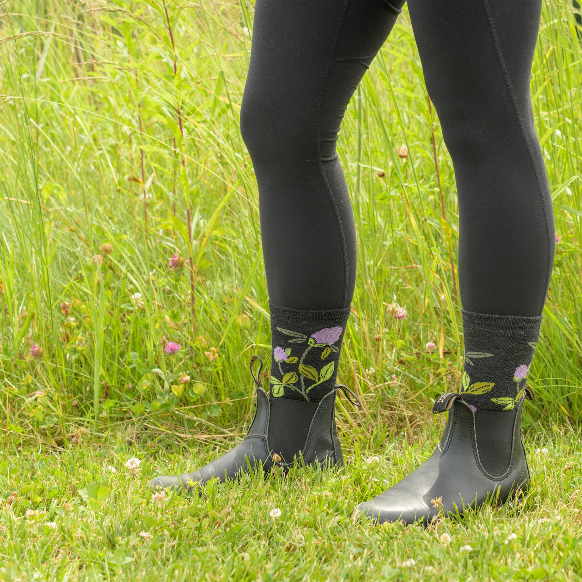 Model wearing charcoal floral crew socks with black ankle boots standing in a grassy meadow