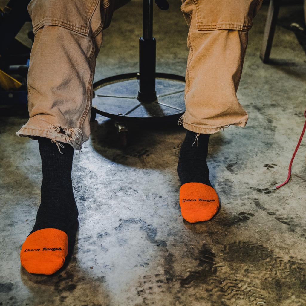 Person seated wearing Darn Tough micro crew socks with bold orange reinforced toe caps