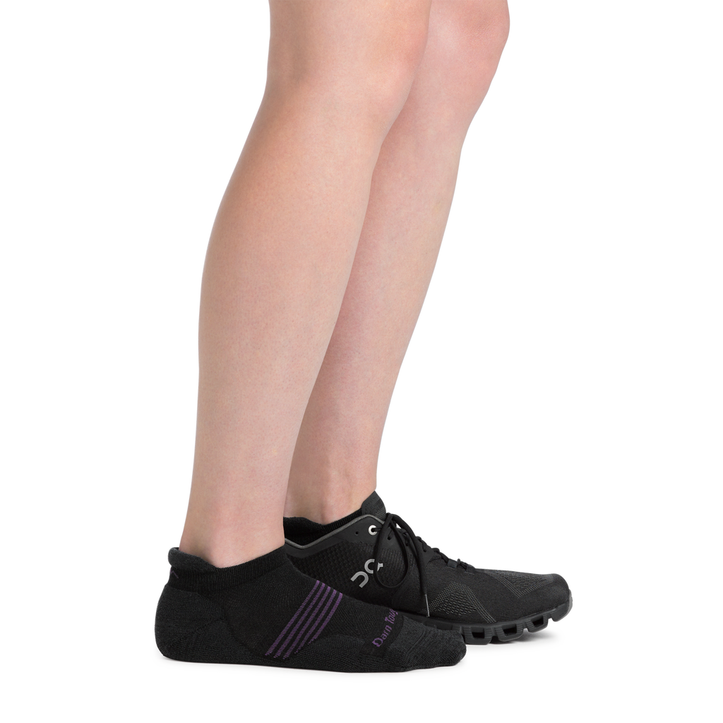 Woman wearing black Darn Tough no-show tab running socks with black athletic sneakers, side view