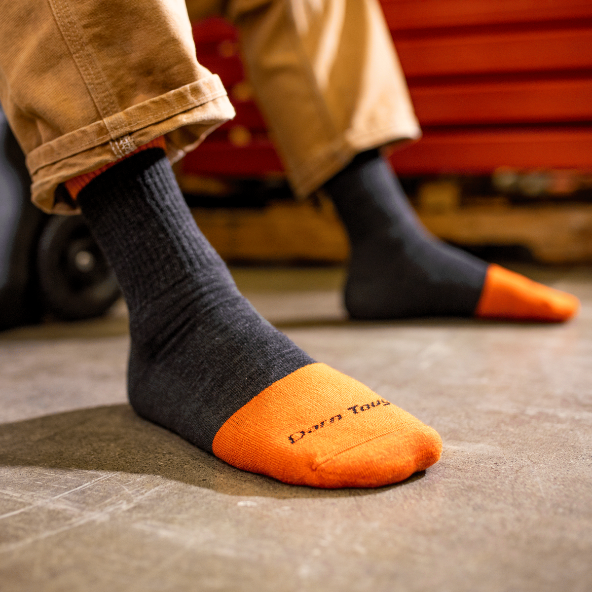 Person wearing dark graphite crew socks with orange reinforced toe cap in workshop setting